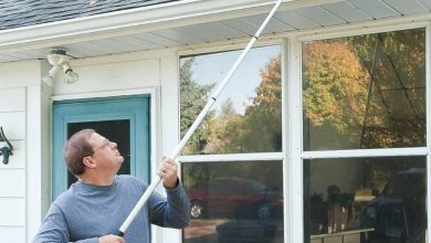 A homeowner safely using a brush on an extension pole to clear light debris from a micro-mesh gutter guard