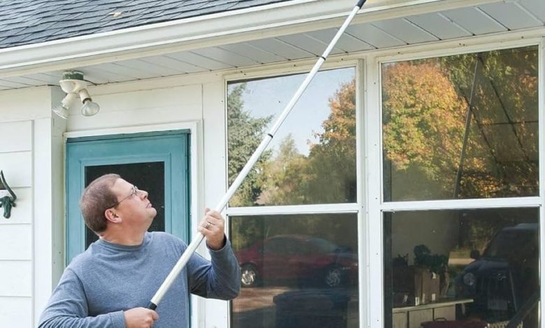 A homeowner safely using a brush on an extension pole to clear light debris from a micro-mesh gutter guard