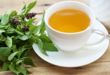 Vibrant green holy basil leaves sit in a white ceramic cup, ready for brewing a calming Tulsi tea
