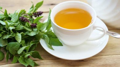 Vibrant green holy basil leaves sit in a white ceramic cup, ready for brewing a calming Tulsi tea