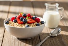 Bowl of plain organic whole grain cereal with fresh berries and milk on wooden table