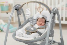 Happy newborn relaxing in plush Ingenuity Swing ‘n Go Deluxe portable baby swing with toy bar