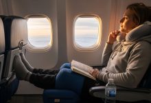 A traveler resting in an airplane seat with a compact orthopedic knee pillow placed under both knees for support during a long flight