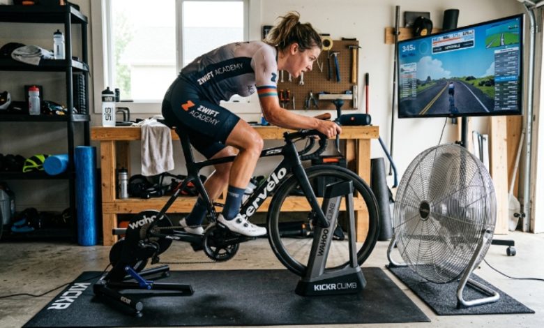 Indoor cyclist training at high intensity on a stationary bike with a large floor fan providing direct airflow in a home gym